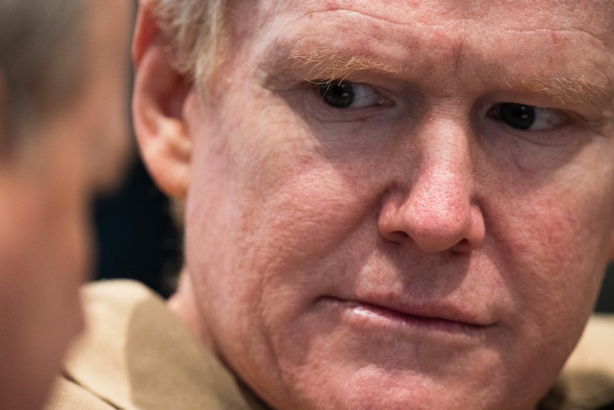 A close up of a man's face in a prison uniform.