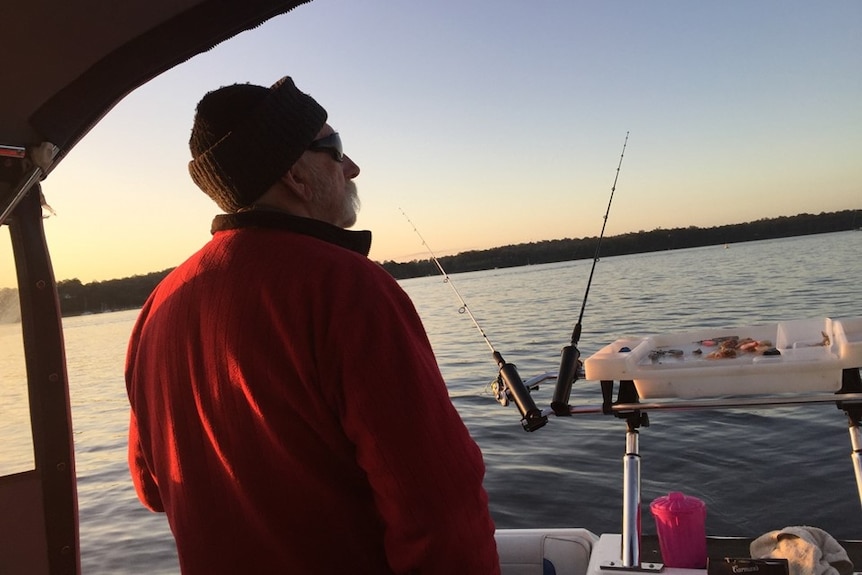 Trevor is on a boat standing next to fishing rods looking towards the sunrise over water