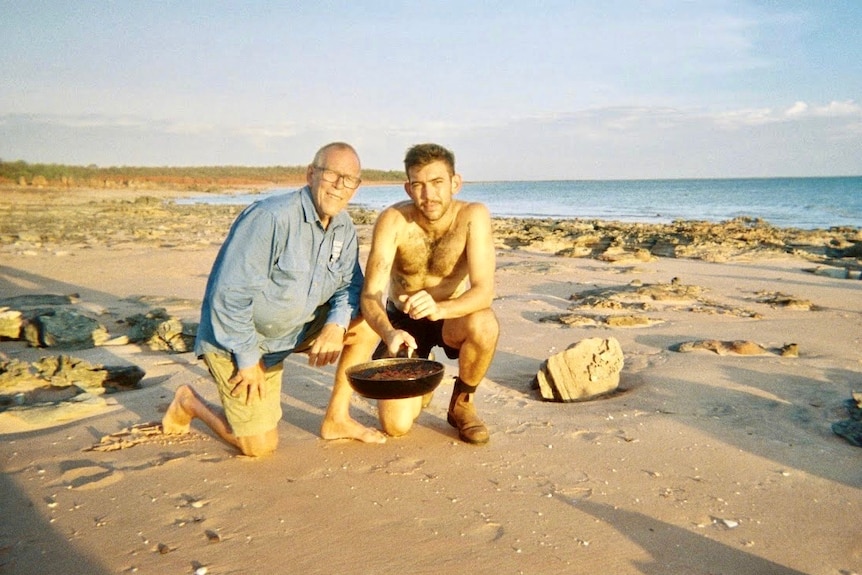 two men kneel on a beach