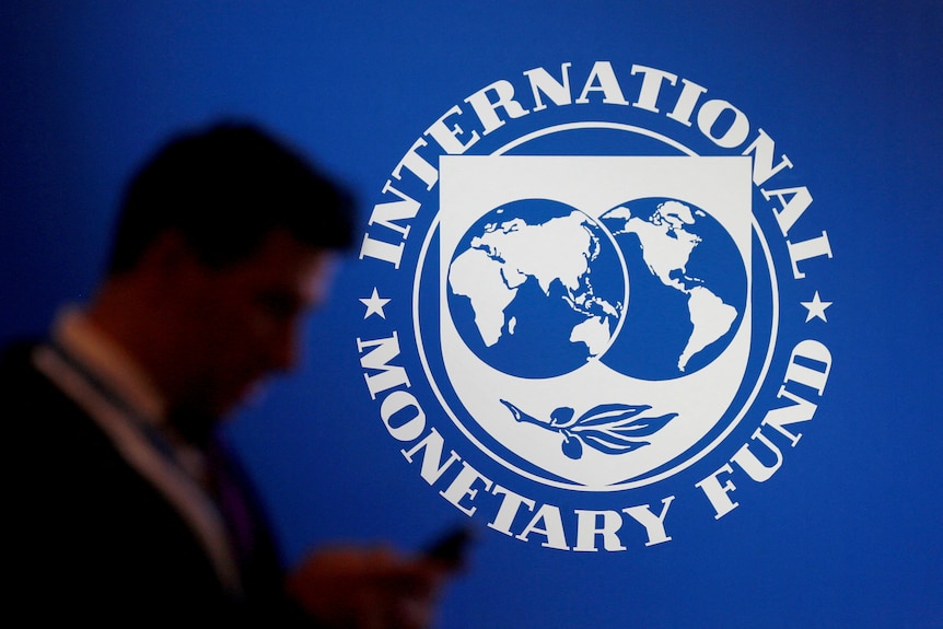 A participant stands near a logo of IMF at the International Monetary Fund - World Bank Annual Meeting