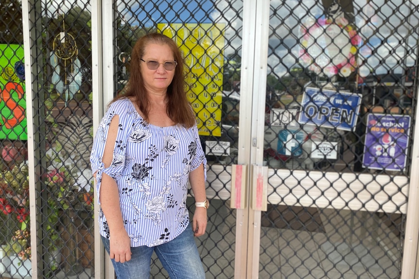 A woman standing outside a florist shielded by mesh wiring.