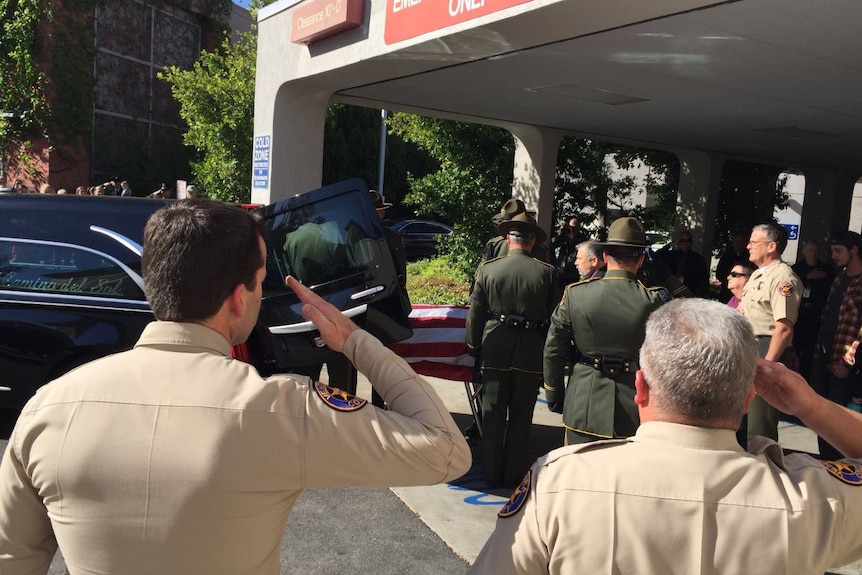 Several law enforcement officers salute as a coffin draped in a US flag is loaded into a hearse.