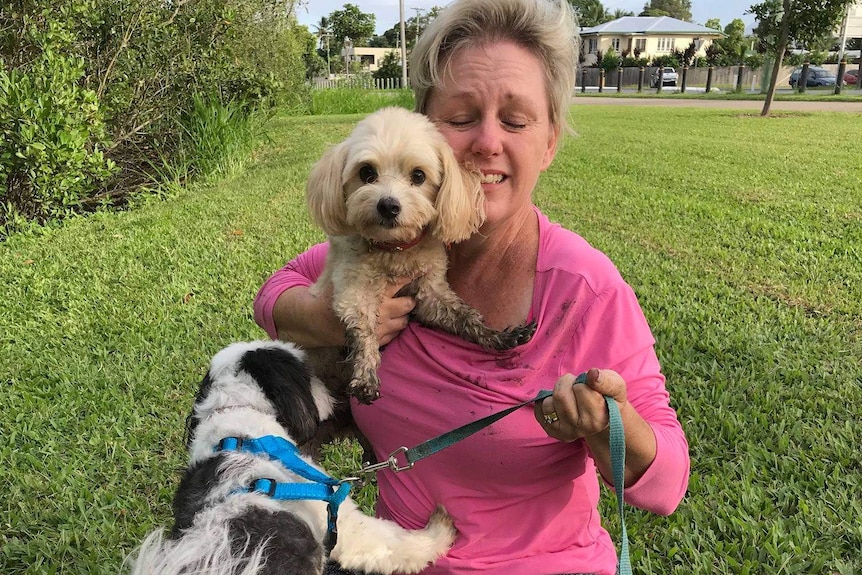 A woman with blonde hair sitting on the grass with two small dogs.