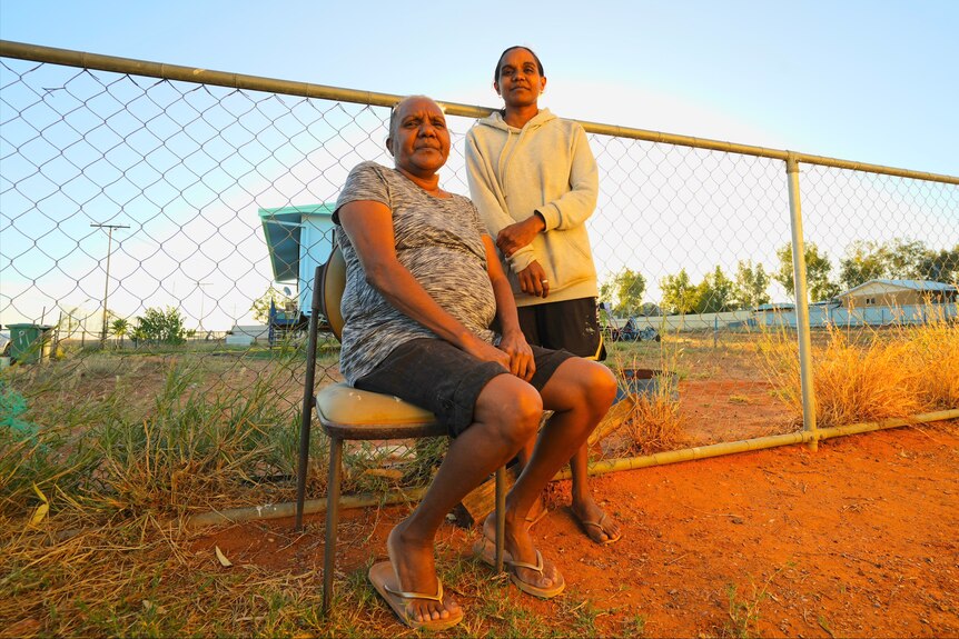 Two women standing by fence with red dirt