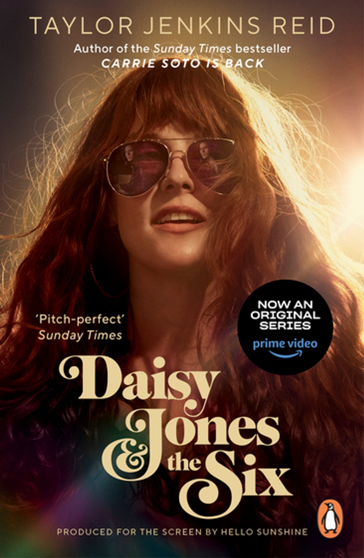 The Daisy Jones book cover, featuring a woman with red hair and sunglasses with a warm spotlight shining behind her.