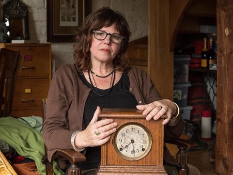 A woman sits in a house, holding an antique clock.