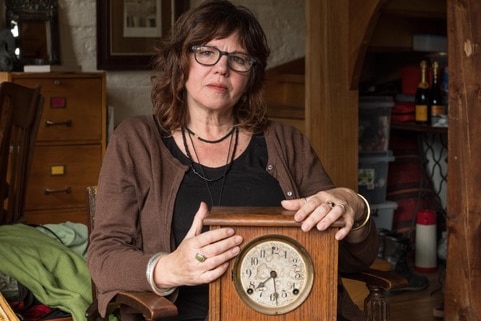 A woman sits in a house, holding an antique clock.