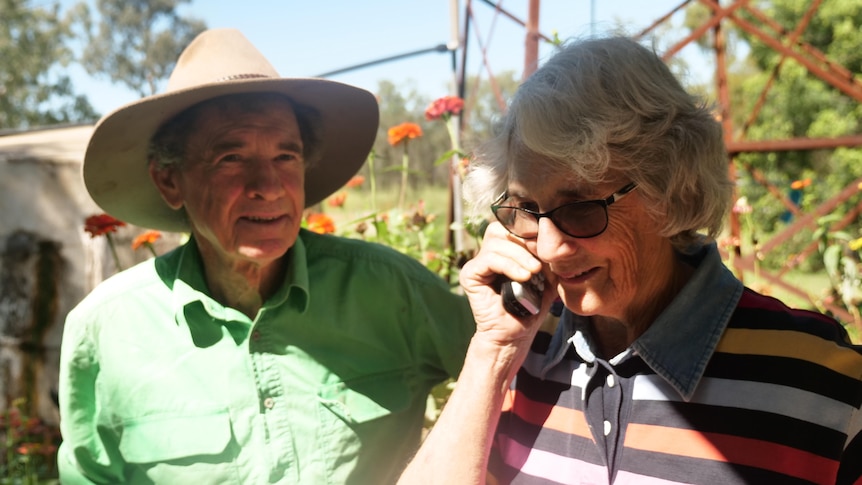 Man and woman standing in a flower garden. The woman holds a mobile phone to her ear.
