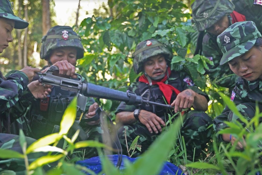 A group of people wearing helmets and uniforms and holding guns stand in a jungle.