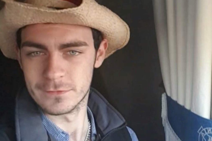 A man wearing a cowboy hat looks at the camera with a beer in his hand.