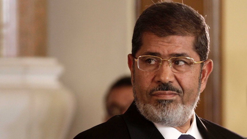 Egyptian President Mohammed Morsi wears glasses and looks over his shoulder