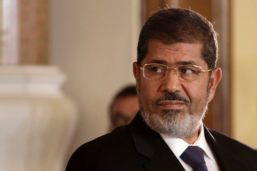 Egyptian President Mohammed Morsi wears glasses and looks over his shoulder