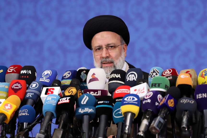 Ebrahim Raisi speaks at a press conference behind a bank of dozens of microphones. 