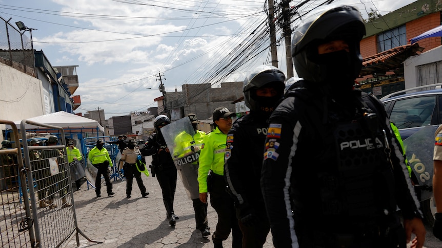 A group of police officers, some in dark uniforms and motorcycle helmets and others in hi-vis, walk down a street.