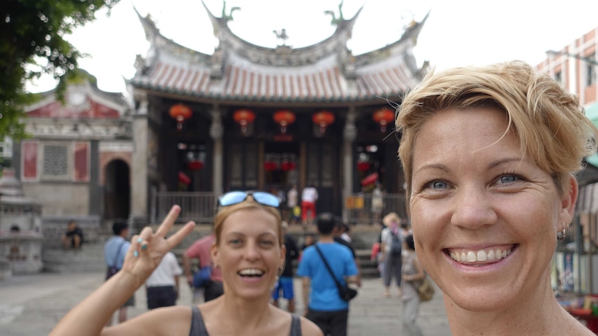 Rachel Davey and Martina Sebova take a photo of themselves in Taiwan with a temple in the background