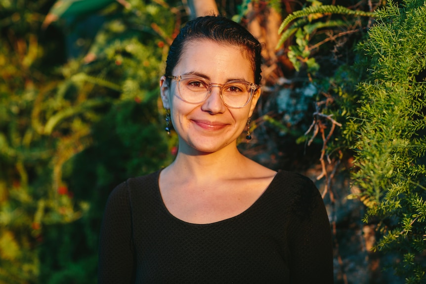 Jewish woman Nicky Gluch wearing glasses and smiling at camera with afternoon sunlight on her faith.