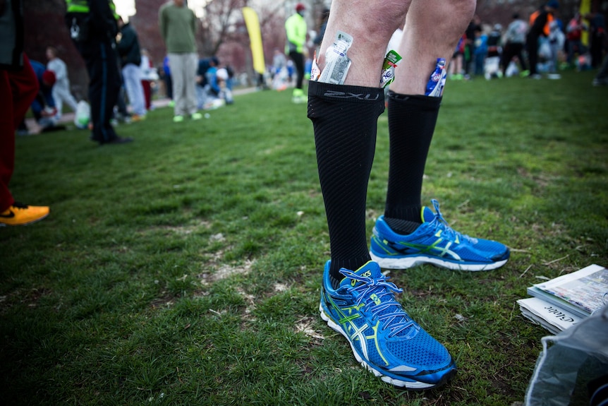 A runner has gel packets tucked into knee length black socks while getting ready to run a marathon.