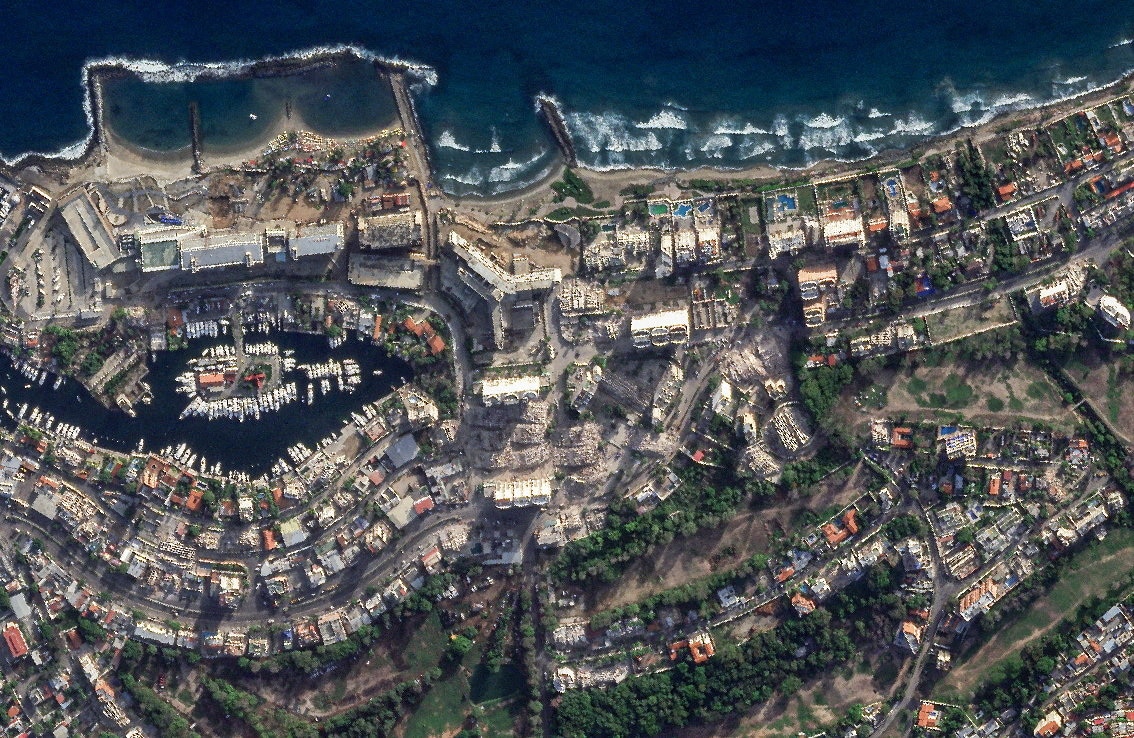 An aerial image of rows of residential homes and an ocean-side boat marina with significant earthquake damage.