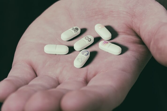Mam's hand holding pills printed with social media logos