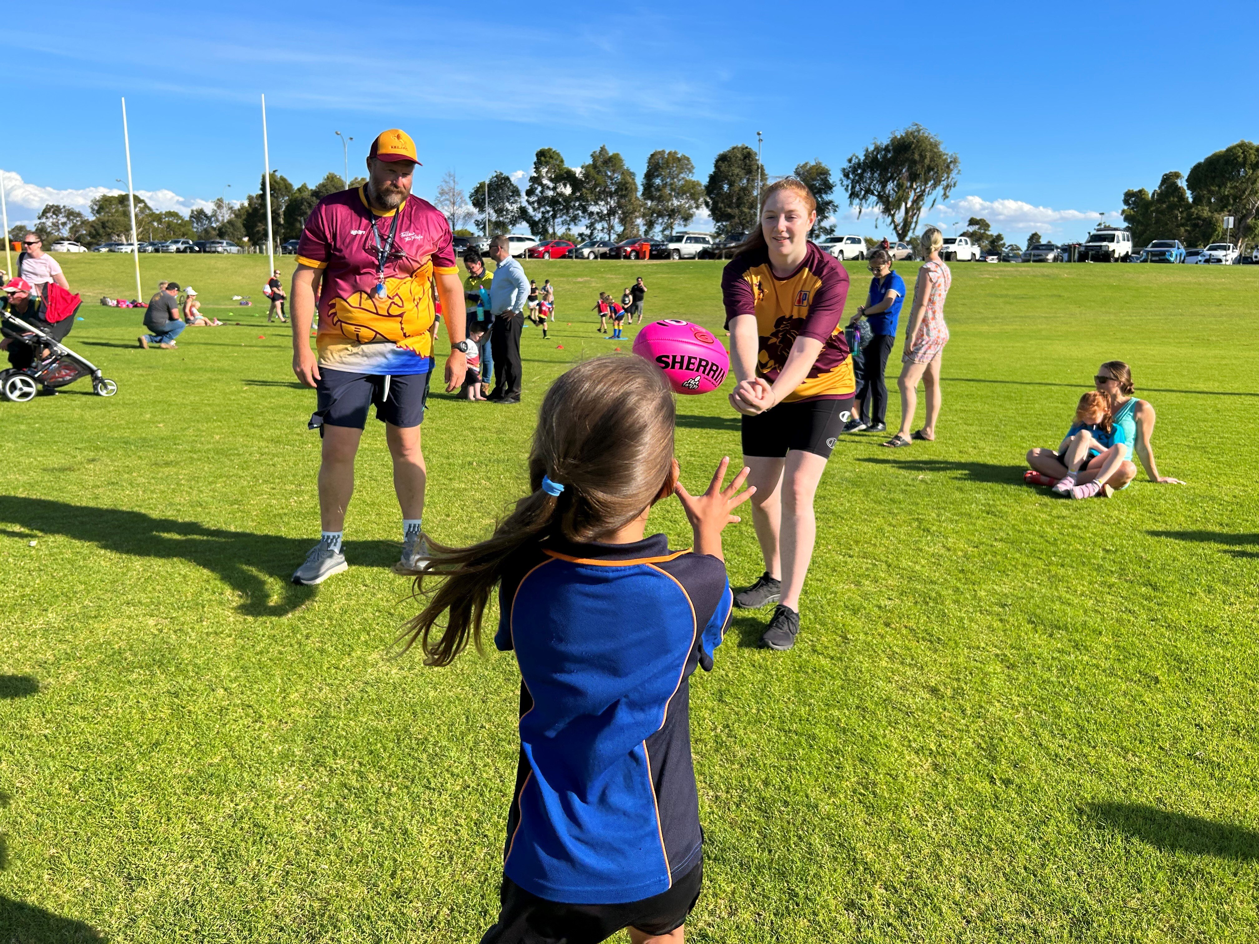 A man and teenage girl throw a pink football towards a young child. 