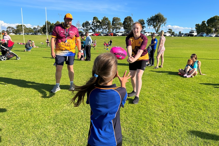 A man and teenage girl throw a pink football towards a young child. 