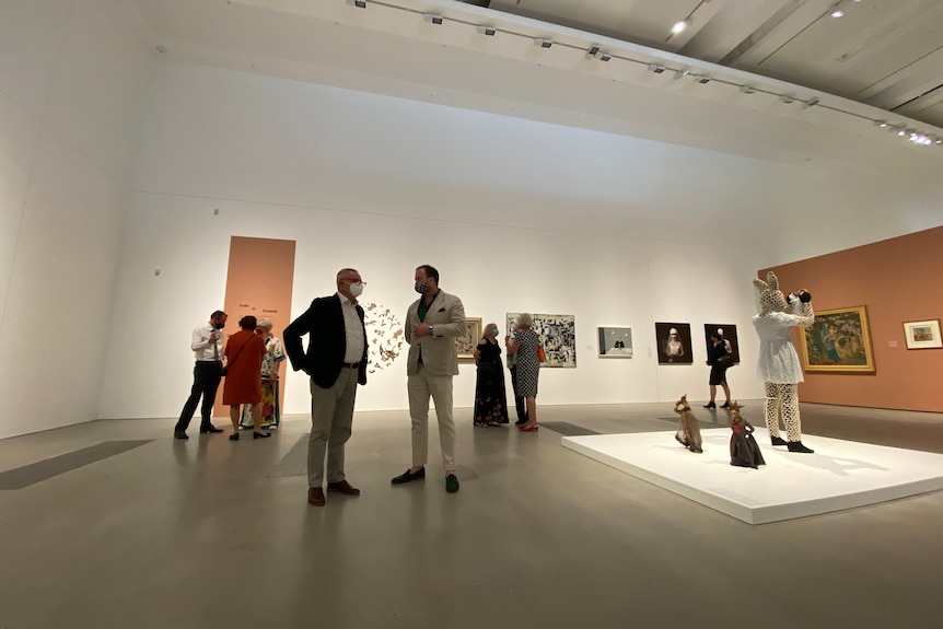 A wide shot showing people standing in groups in an art gallery space. 