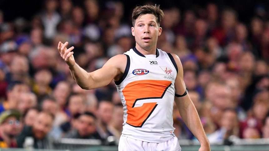 A male AFL player raises his right hand as he looks to his right.