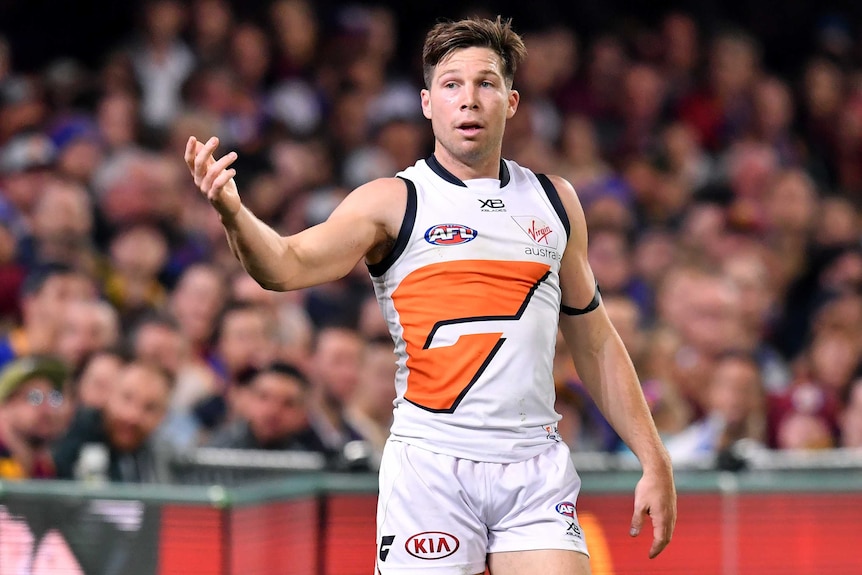 A male AFL player raises his right hand as he looks to his right.