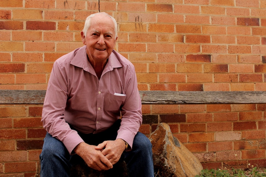 A man sits in front of a brick wall