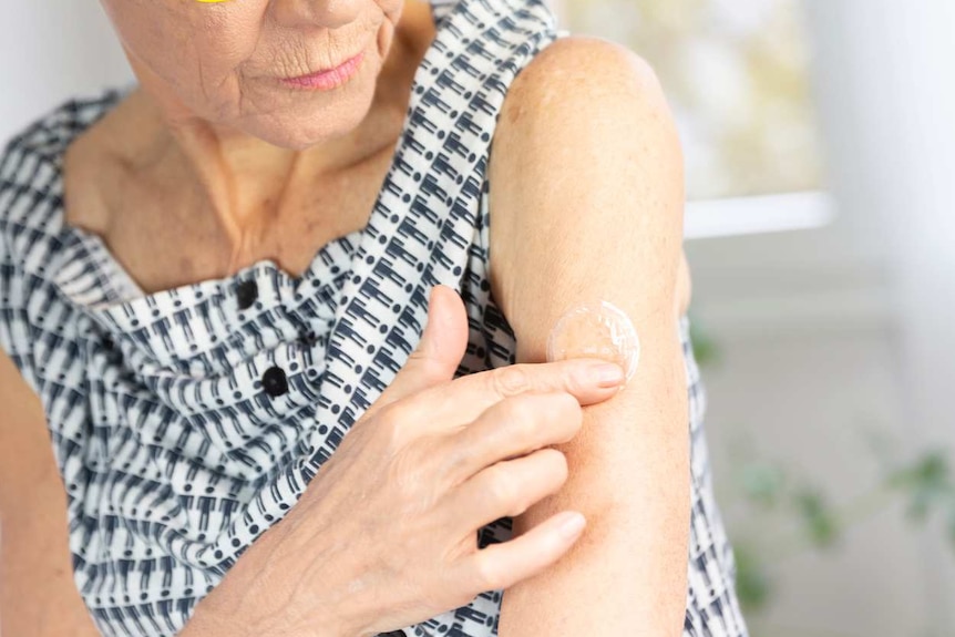 An older woman rubs a gel onto the skin of her upper arm.