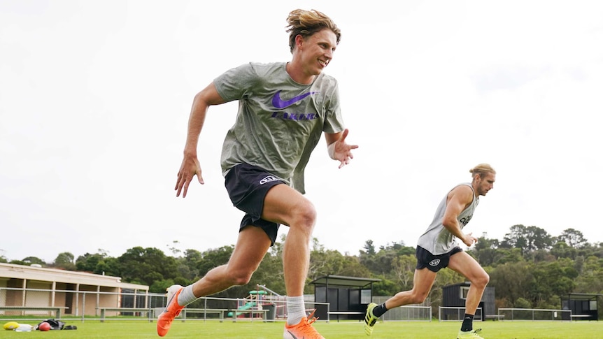 Two AFL footballers sprint together, metres apart, during training in coronavirus isolation.