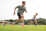 Two AFL footballers sprint together, metres apart, during training in coronavirus isolation.