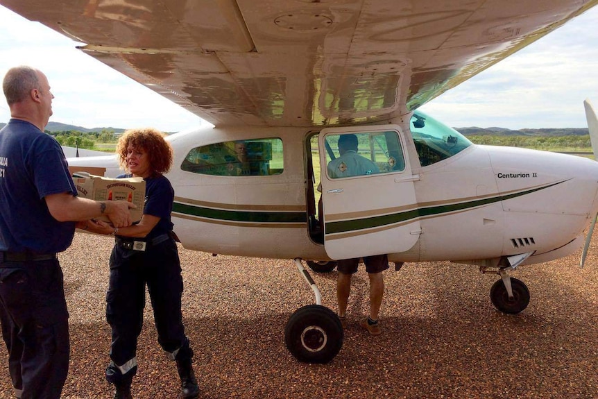 A man hands a box to a woman next to a small plane.