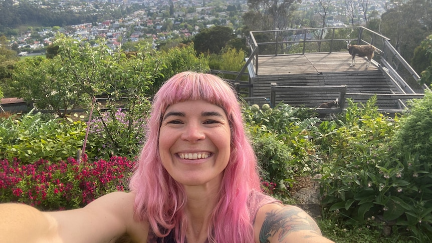 Hannah Moloney takes a selfie outside near nipaluna/Hobart. The garden, a deck and goat in the background.