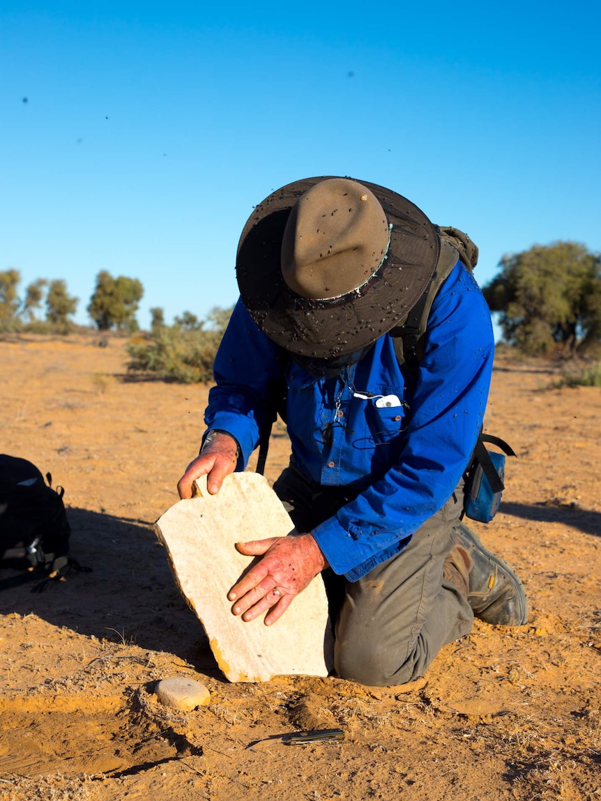 Man holding a large grinding stone.