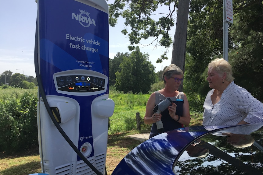 Two women talk next to an NRMA charging station 