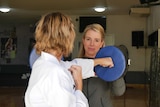 A woman in a taekwondo uniform punches a boxing pad.