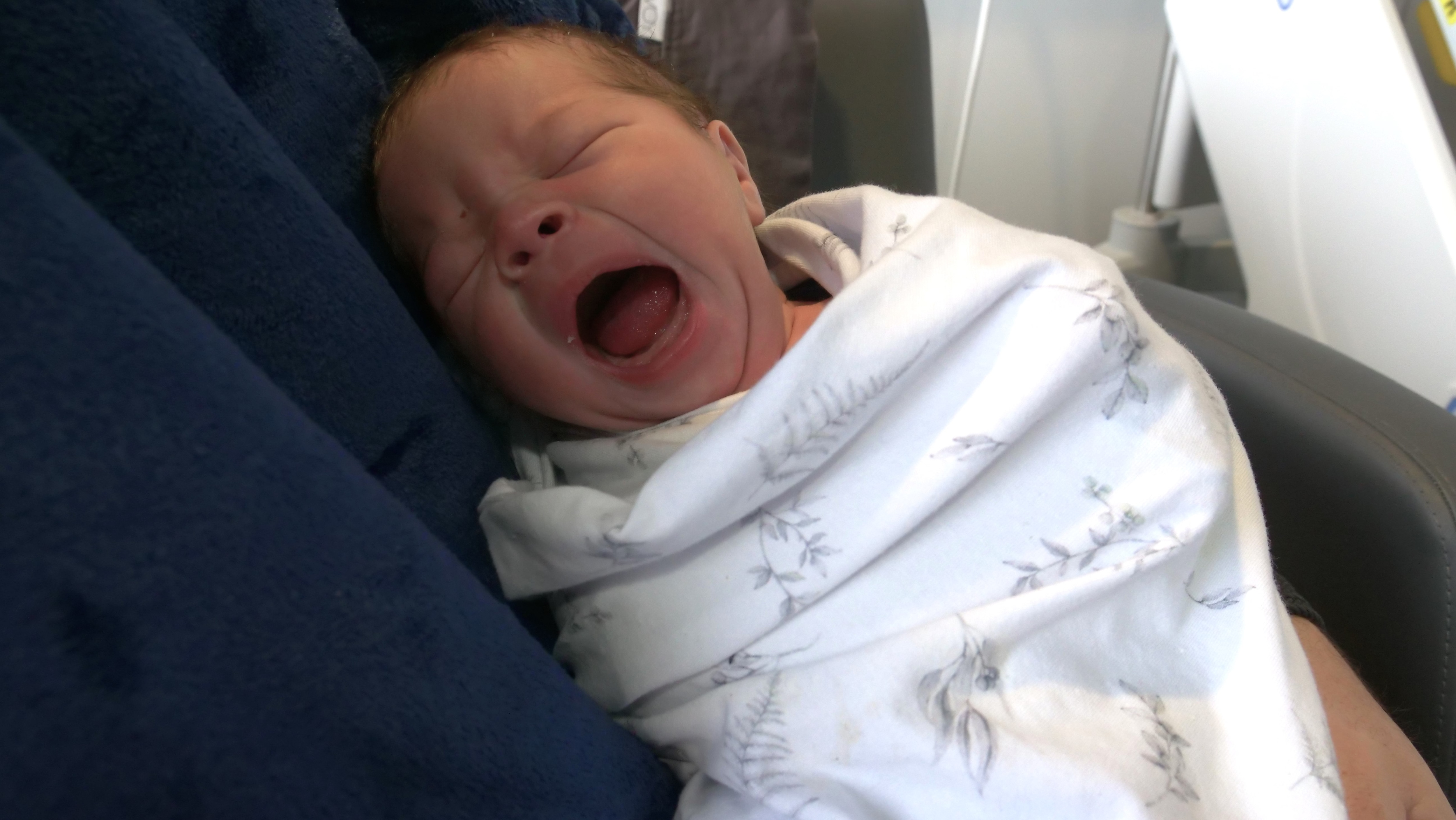 A baby in a wrap yawning with its mouth open really wide.