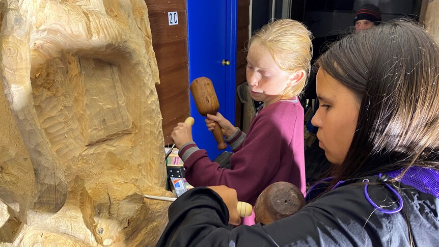 A close up of students carving a tree trunk. 