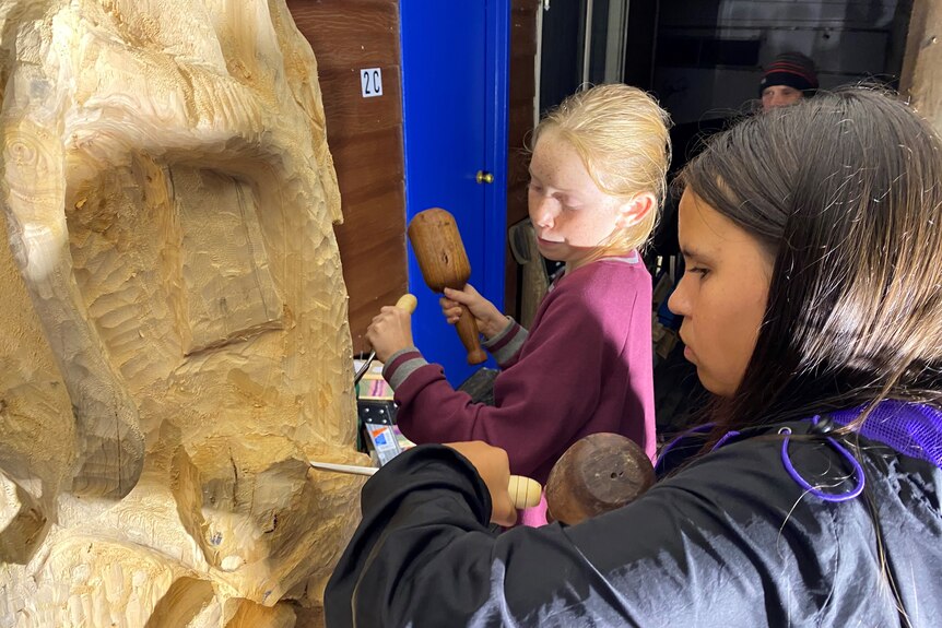 Students carve a tree trunk. 