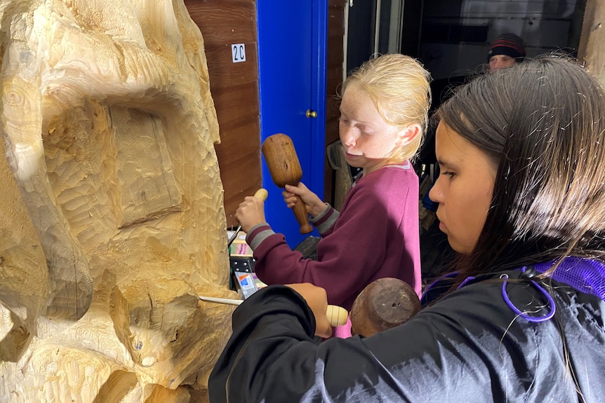 A close up of students carving a tree trunk. 