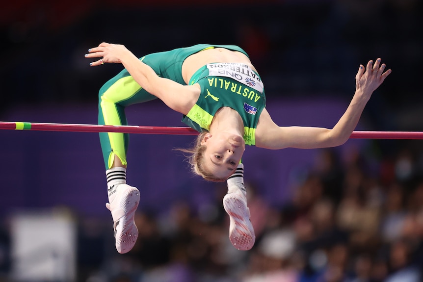 A woman wearing green and yellow flips backwards over a pole