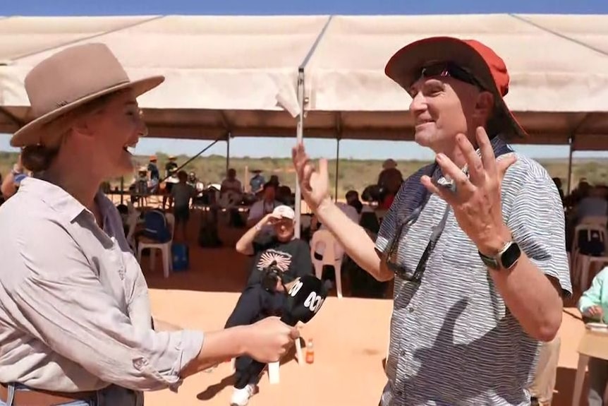 A man gestures in amazement while talking to an ABC presenter in the desert.