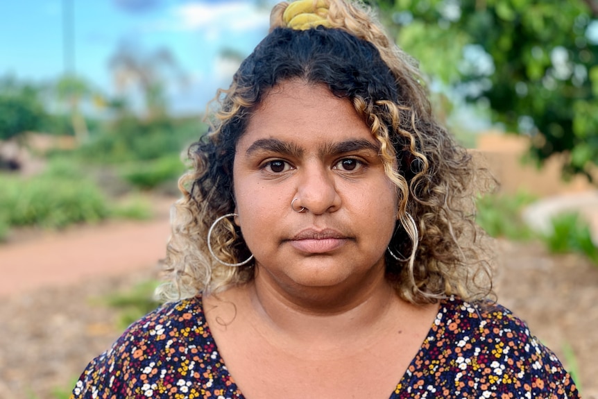 A woman with olive skin and curly hair stares directly down the camera lense.