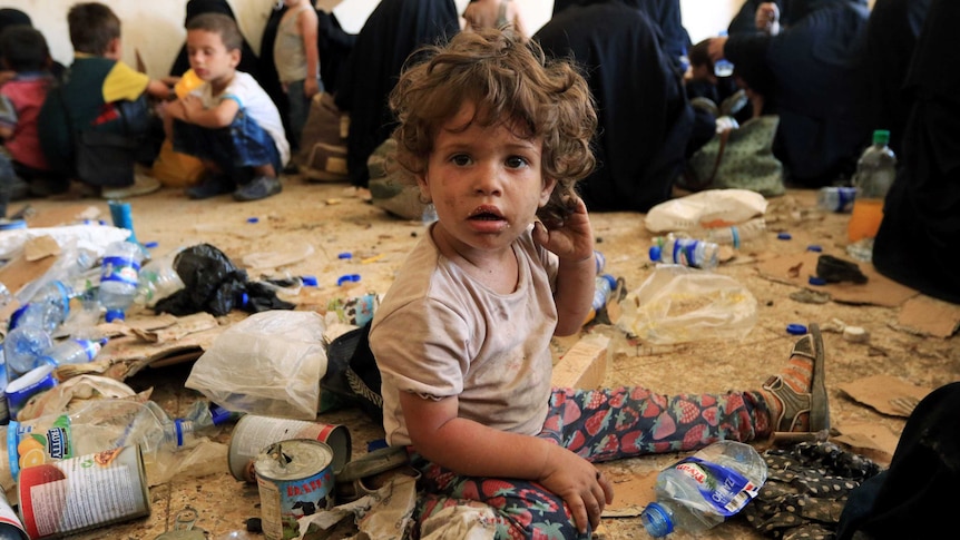 A toddler covered in dirt sits amongst piles of rubbish.