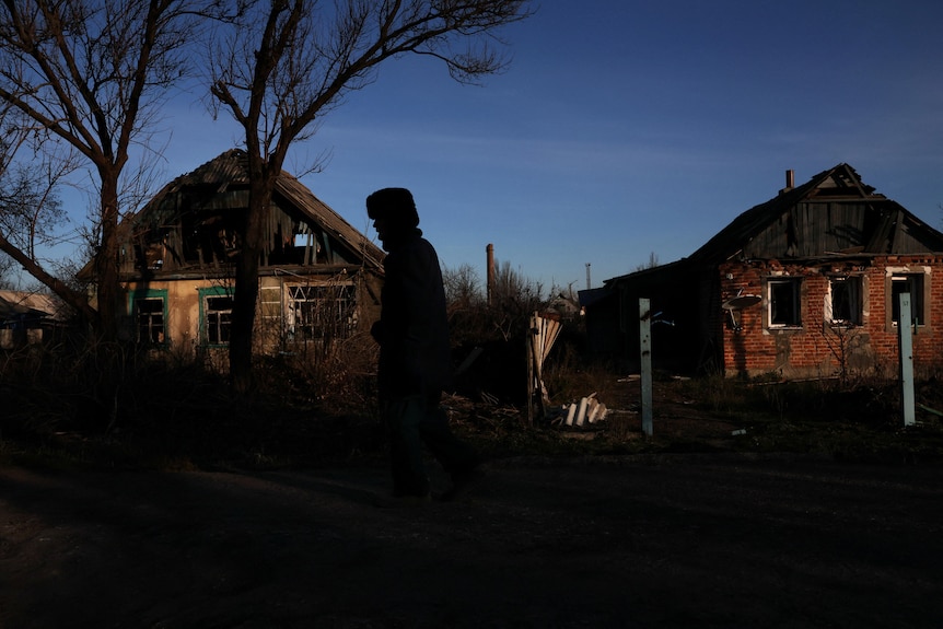 a man's silhouette can be seen as he walks down a street with damaged houses behind him