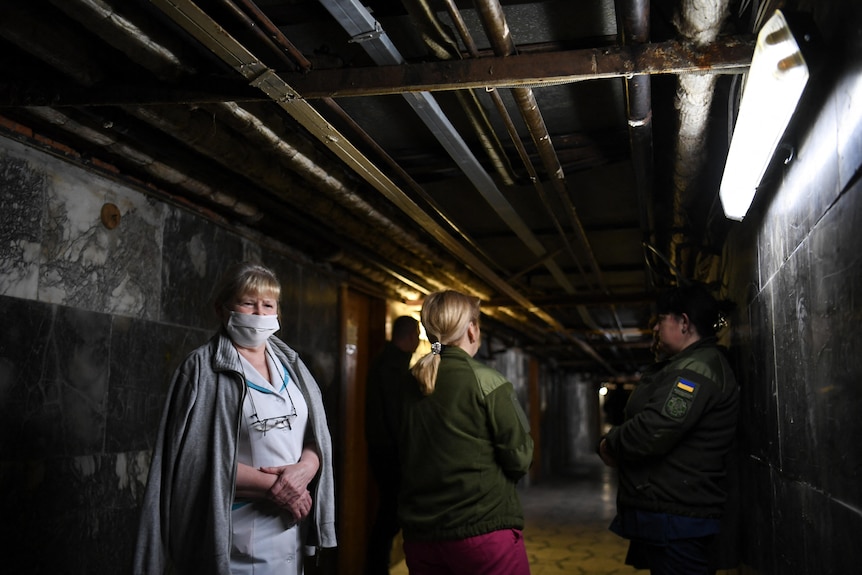 A woman in a medical mask stands in an underground hallway, with a group of people