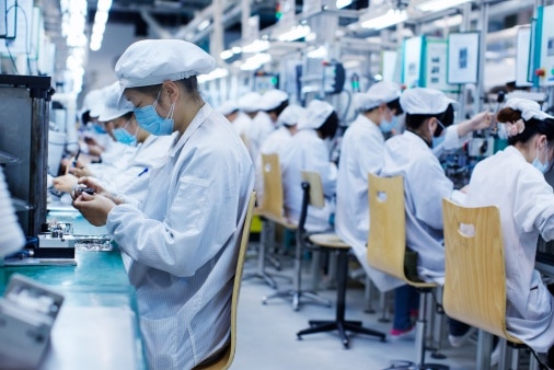 Group of workers at small parts manufacturing factory in China, wearing protective clothing, hats and masks.