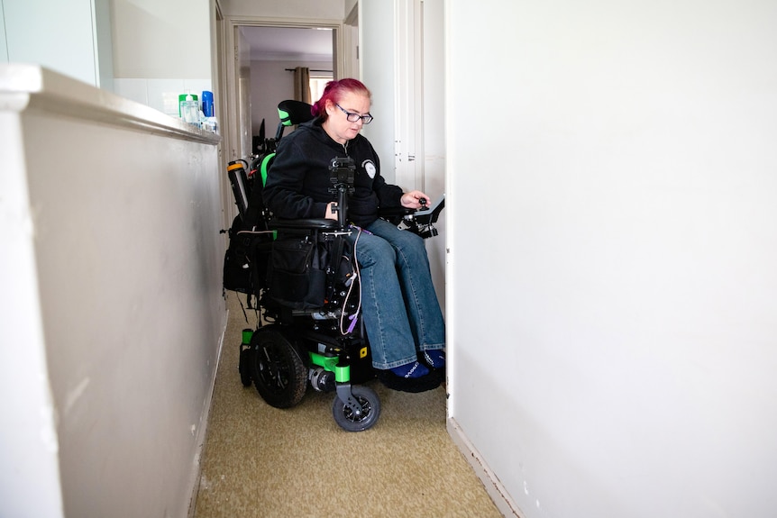 A woman tries to negotiate a narrow hallway in her wheelchair.