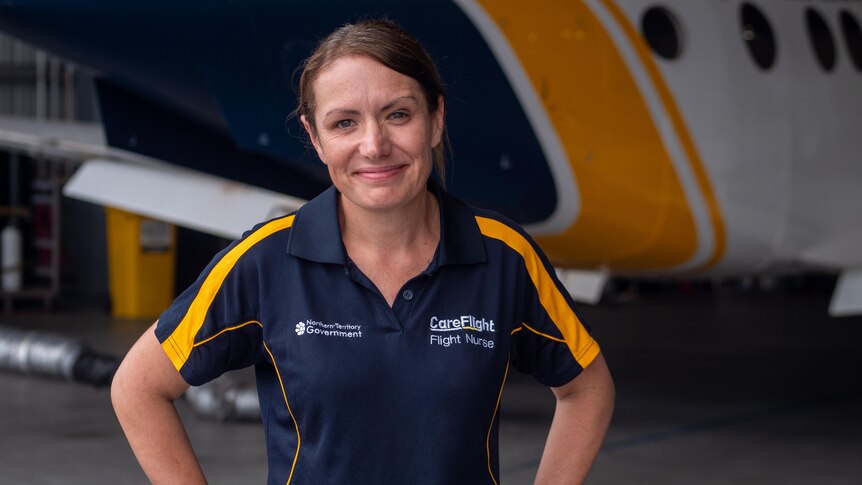 A woman in short sleeve polo work shirt beside a small plane in a hanger.
